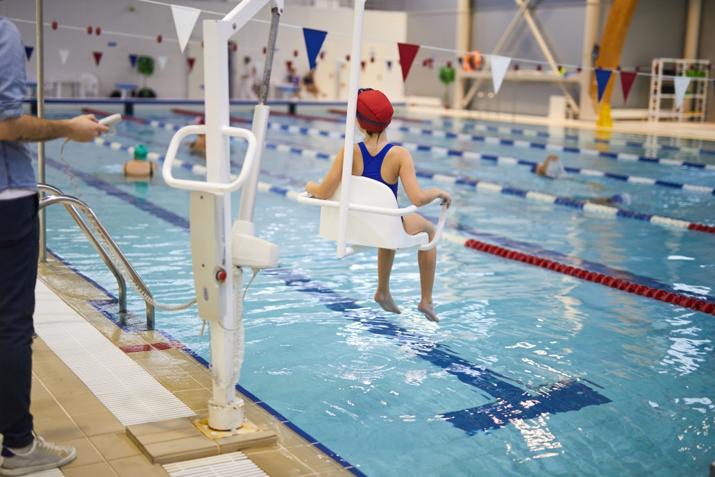 Infante accede a la piscina mediante una silla salvaescaleras acuática.